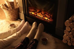 Image of 2 people warming their feet by a fireplace- Chimney Maintenance and Fireplace Safety blog featured image