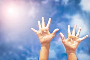2 hands against the sunny sky with sunscreen smiley faces- Sun Safety blog featured image