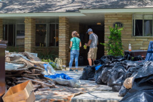 A man and woman cleaning up their house after a hurricane- What to Do After a Hurricane blog featured image