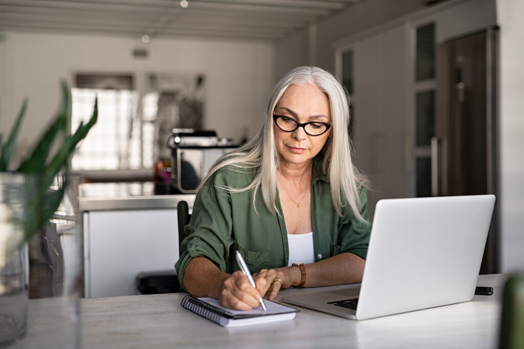 Senior woman with her laptop open, writing something down- Medicare Supplement Plan blog featured image