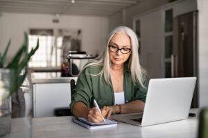 Senior woman with her laptop open, writing something down- Medicare Supplement Plan blog featured image